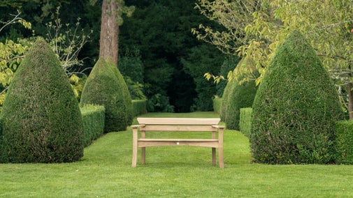 Oak bench placed in a large garden with tree's surrounding
